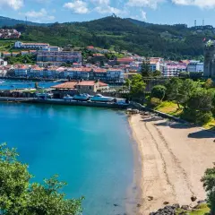 Bahía con barcos y un pueblo costero al fondo. Ideal para planificar como viajar barato por España y disfrutar de sus costas.