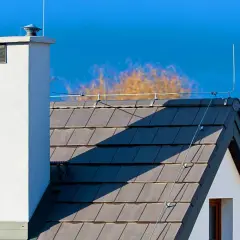 Instalacja odgromowa na dachu z kominem, zgodnie z przepisami, chroni dom przed uderzeniem pioruna.
