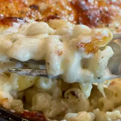 Un tenedor levanta una porción cremosa de macarrones con queso horneados, con la parte superior dorada y burbujeante.