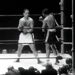 Two boxers in a ring. One boxer, possibly Rocky Marciano, is in the foreground, his reach evident as he prepares to strike.