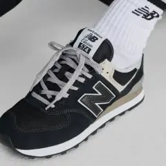 Klasyczne czarne buty sportowe new balance wl 574 z szarymi sznurówkami i beżowymi akcentami, noszone z białymi skarpetkami z logo.