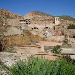 Ruinas de las minas Rodalquilar, con edificios abandonados y balsas circulares en un paisaje árido bajo un cielo azul.