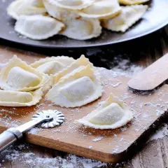 Raviolis frais sur une planche à découper avec une roulette à pâtisserie et une spatule.