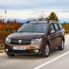 Brązowy Dacia Logan MCV jedzie po krętej drodze wśród jesiennych drzew i gór w tle.