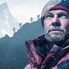Zmęczony alpinista w czapce i kurtce patrzy w górę. W tle widać innych wspinaczy na zboczu podczas wyprawy na Broad Peak.