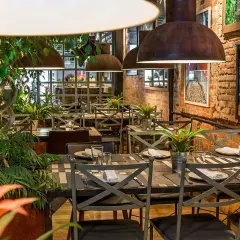 Tavoli apparecchiati in un ristorante con piante rigogliose e foto di frutta. Un'ottima opzione per sapere dove mangiare a Madrid.