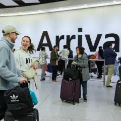 Para podróżnych z bagażami na lotnisku Heathrow, na tle napisu "Arrivals".