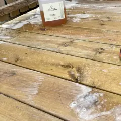 En flaska såpa står på en altan med såpskum. En svart stövel med orange kant syns i nedre högra hörnet.