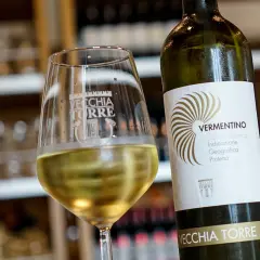 Un bicchiere di vino bianco, il vermentino è frizzante, accanto alla bottiglia Vecchia Torre.