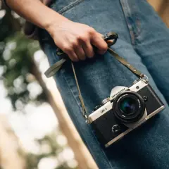 Dłoń trzyma aparat OM-3, przypominając o czasach, kiedy powstał aparat fotograficzny.