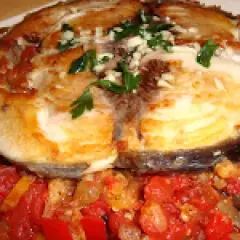 Rodaja de pescado blanco, posiblemente mero, servida sobre un sofrito de verduras y hierbas. Un delicioso plato de sam de atún.