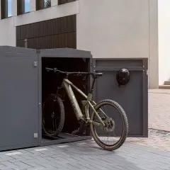 Ein grünes Mountainbike steht in einem modernen, grauen Fahrrad-Stellplatz. Ein Helm hängt an der Tür.