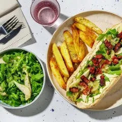 En härlig fransk mat-inspirerad måltid med en baguette fylld med krämig sås, ruccola, päron och knaprigt bacon, serverad med klyftpotatis och en fräsch sallad.