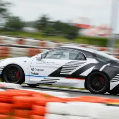 Biało-czarne Alpine A110 z logotypami Castrol i Delphi pędzi po torze wyścigowym, zostawiając za sobą rozmyte bariery.