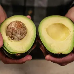 Dłonie trzymają połówki awokado. Jedna z nich ma pestkę, druga jest pusta. Idealne do guacamole, gdy wiesz, jak zmiękczyć awokado.