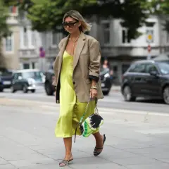 Elegancka, satynowa sukienka dla figury jabłko w jaskrawym kolorze, zestawiona z beżową marynarką i stylową torebką.