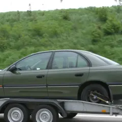 Zielony samochód na lawecie, w tle zielone wzgórze.