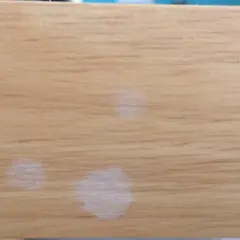 Trois petites taches blanches sur une surface en bois clair, comme des traces laissées par des gouttes d'eau séchées.