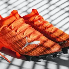 Pomarańczowe korki piłkarskie Puma z napisem "CONTROL PRO". Różnice między korkami profesjonalnymi a amatorskimi są widoczne w technologii i materiałach.