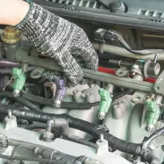 Main d'un mécanicien ganté manipulant le rail d'injection pour tester injecteur diesel.