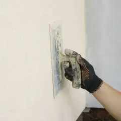 Ręka w rękawicy nakłada tynk kornik na ścianę, tworząc charakterystyczną fakturę.