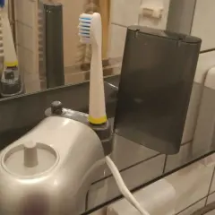 Elektroniczna szczoteczka do zębów i jej wymienna końcówka stoją na szklanej półce, pokazując, jak przechowywać szczoteczki do zębów w łazience.