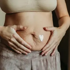 Kobieta z kremem w kształcie serca na brzuchu, szukająca domowych sposobów na obkurczanie macicy.