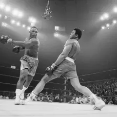 Two boxers clash in a dramatic moment. One out boxer throws a punch while the other dodges, the crowd watching intently.