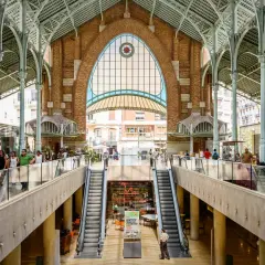 Interior del Mercado de Colón, con sus arcos de hierro y cristal, escaleras mecánicas y puestos de comida.