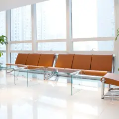 Moderna sala d'attesa con divani in pelle color cuoio, tavolini in vetro e piante verdi. Ottime idee per una sala d'attesa accogliente e di design.
