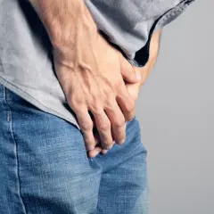 Dłoń mężczyzny w dżinsach i szarej koszulce, czuje dyskomfort, jakby pojawiły się grudki perliste.