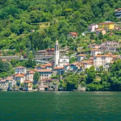 Ein malerisches Dorf am Nesso Comer See, mit traditionellen Häusern, die sich an den grünen Hang schmiegen.