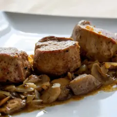 Soczyste polędwiczki w sosie pieczarkowym, podane na białym talerzu. Aromatyczny sos z pieczarkami i cebulką otula delikatne mięso.