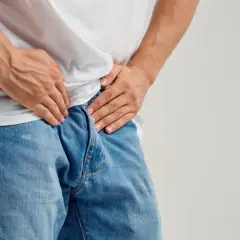 Mężczyzna w dżinsach i białej koszulce, trzymający się za krocze. Obraz symbolizuje obawy związane z rakiem prostaty i przerzutami.