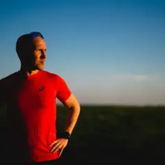 Mężczyzna w czerwonej koszulce, z okularami na głowie, patrzy w bok na tle błękitnego nieba. To ważny tekst dla biegacza.