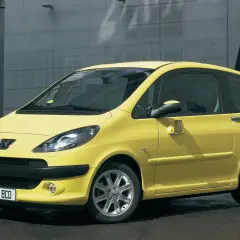 Żółty Peugeot 1007 z przesuwnymi drzwiami na tle nowoczesnego budynku.