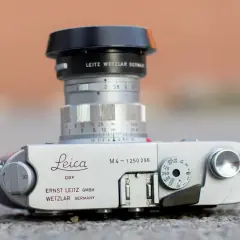A Leica M4 camera with a Leitz Wetzlar lens. The camera body shows "Leica M4" and "Ernst Leitz GmbH Wetzlar Germany." The lens has aperture markings and a focus ring. The framelines are not visible in this shot.
