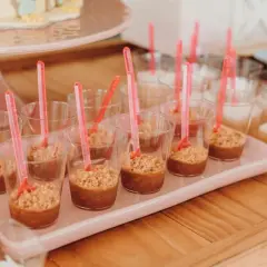Słodkości na urodziny w restauracji: małe deserki w kubeczkach z różowymi łyżeczkami.