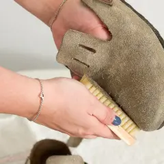 Hände reinigen Wildlederschuh mit Bürste. So lassen sich hartnäckige blutflecken aus leder entfernen und das Material wird wieder wie neu.