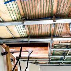 Widok sufitu podwieszanego z widocznymi instalacjami. Widać metalowe profile, wełnę mineralną, rurki systemu ogrzewania podłogowego i elementy konstrukcyjne. Maty kapilarne wady nie są widoczne.