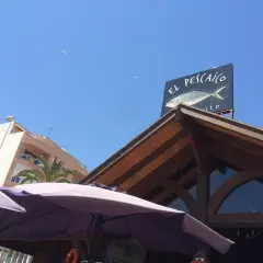 Un cartel de "El Pescaito" con un dibujo de pez, bajo un cielo azul con gaviotas.