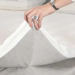Hände ziehen den Reißverschluss eines Toppers ab, um die **Boxspringbett Pflege** zu erleichtern.
