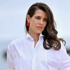 Carlota de Monaco, con pendientes rojos y camisa blanca, mira a lo lejos.