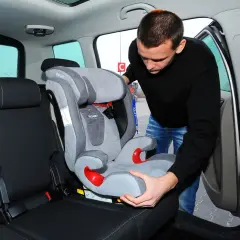 Mężczyzna montuje fotelik samochodowy na bazie Isofix. Czy baza Isofix pasuje do każdego fotelika? Sprawdźmy!