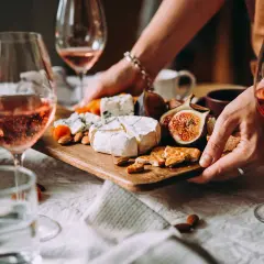 Gemütliche weinverkostung zu hause mit Roséwein, Käse, Feigen und Nüssen auf einem Holzteller.