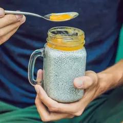 Mann hält ein Glas Chia-Pudding mit Mango-Topping. Die Frage "wieviel chiasamen pro tag" wird durch die gesunde Mahlzeit beantwortet.