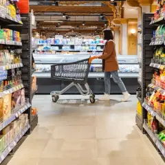 Kobieta z wózkiem w sklepie, między regałami pełnymi produktów. Może szuka jakiegoś dobrego **brendi** na prezent.
