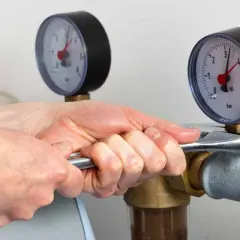 Mains de technicien ajustant un raccord sur un tuyau, près de manomètres. Installation d'un adoucisseur électromagnétique.