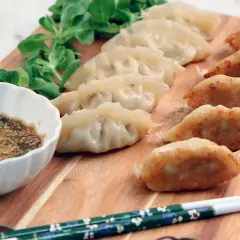 Stekta och ångade dumplings på en träbricka med dippsås och grönsaker. Ett perfekt dumplings recept för en god måltid.