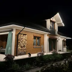 Nowoczesna iluminacja podkreśla architekturę domu i ogród. Wzdłuż dachu biegną świetlne linie, tworząc efektowną **modernizację oświetlenia**.